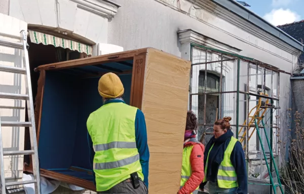 3 personnes sortent un meuble par la fenêtre d'un logement.